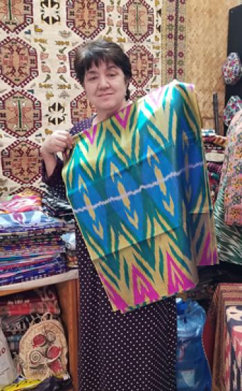 Shop owner Zulfiya Yusupova holding up an antique ikat-design robe — Minzifa Boutique of Applied Arts, Bukhara. Photo by Edna R.S. Alvarez