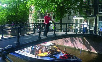 Thea Ramsay on a bridge over the Brouwersgracht as a canal-tour boat passes beneath — Amsterdam.