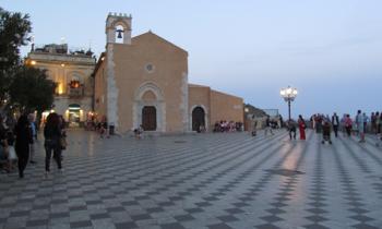 Visitors strolling, at dusk, past Sant’Agostino church in Taormina’s Piazza IX Aprile.