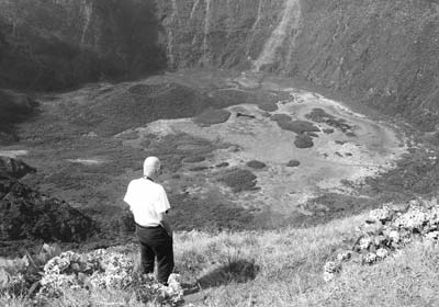 A hiker peers into a green crater a mile wide and 1,300 feet deep on Faial.