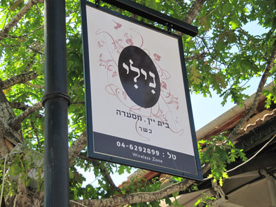 The sign for a restaurant across the street from the museum. It reads “NILI — Beit yayin Mesadah,” literally, “NILI — House of Wine Restaurant,” with the phone number at the bottom.