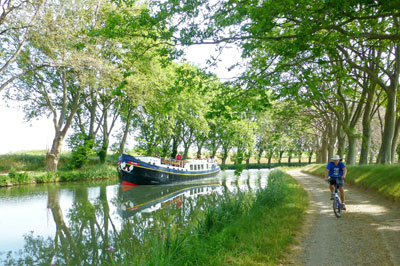 Randy Keck riding a bike on a towpath of the Canal du Midi as the luxury barge Anjodi cruises along. Photo by Gail Keck