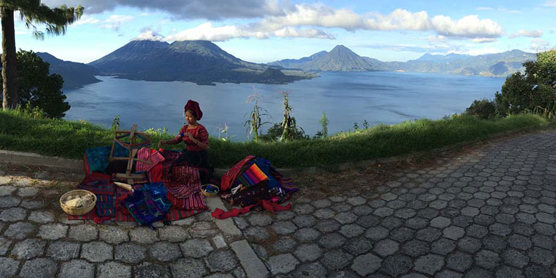 Maria, our guide at Lake Atitlán, sitting at a loom in front of the dramatic landscape.