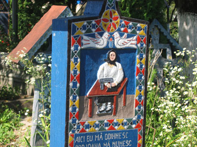 A carved wooden tombstone depicting a woman at a sewing machine — Merry Cemetery, Sapânta, Romania. Photo by Bob Derge