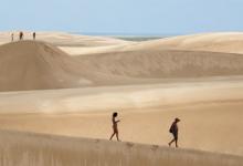 Swirls of white sand flow across the dunes, dwarfing hikers in Lençóis Maranhens